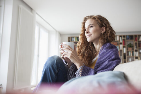 Frau zu Hause auf der Couch sitzend mit Tasse - RBF003091