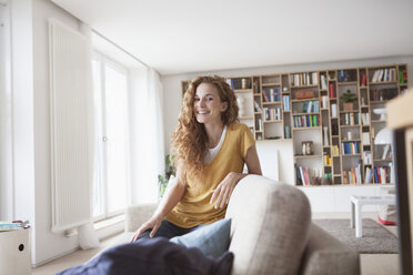 Lächelnde Frau zu Hause auf der Couch kniend - RBF003094