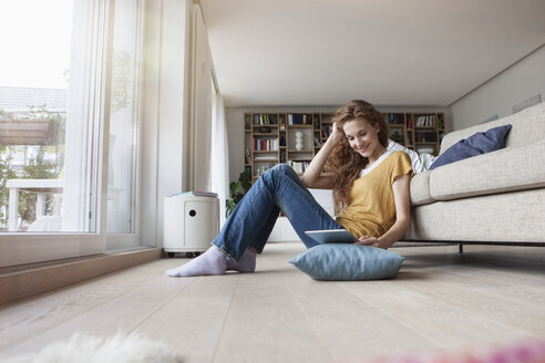 Woman at home sitting on floor holding digital tablet - RBF003102