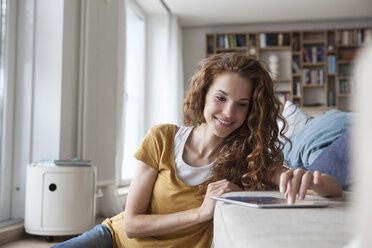 Smiling woman at home using digital tablet on couch - RBF003107