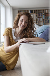 Smiling woman at home using digital tablet on couch - RBF003108