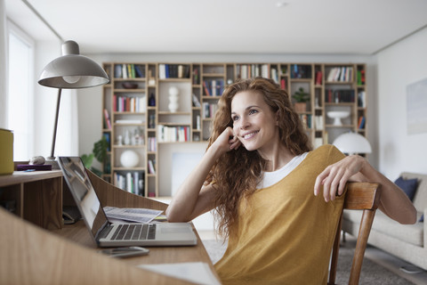 Smiling woman at home with laptop on secretary desk stock photo