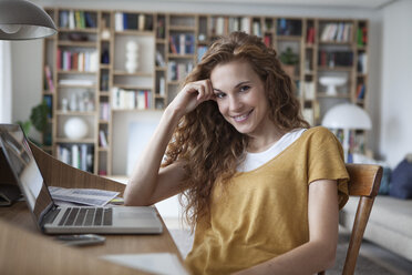 Smiling woman at home with laptop on secretary desk - RBF003113