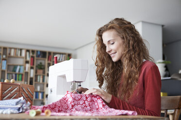 Smiling woman at home using sewing machine - RBF003115