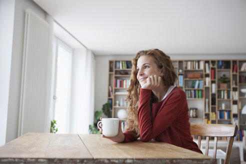 Lächelnde Frau zu Hause sitzt am Holztisch mit Tasse - RBF003118