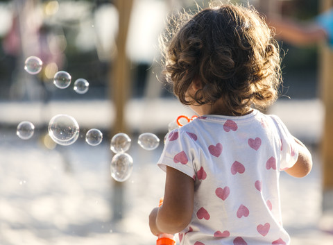 Back view of little girl making soap bubbles at playground stock photo