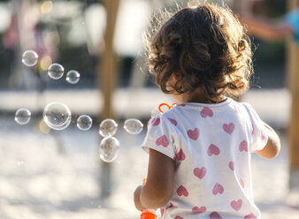 Rückansicht eines kleinen Mädchens, das auf einem Spielplatz Seifenblasen macht - MGOF000479