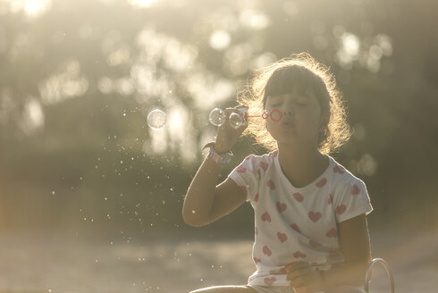 Little girl making soap bubbles in the park at twilight - MGOF000482