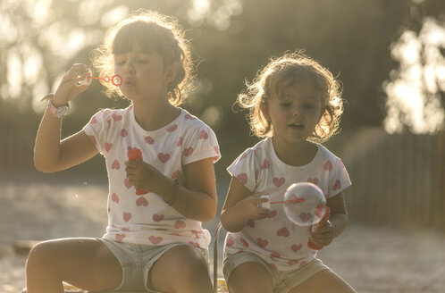 Zwei kleine Schwestern machen Seifenblasen im Park in der Dämmerung - MGOF000484
