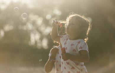 Two little sisters making soap bubbles in the park at twilight - MGOF000485