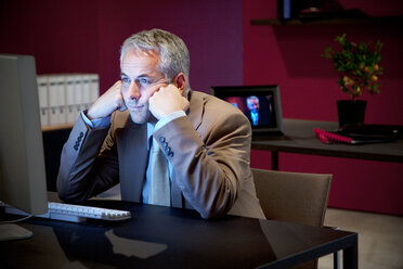 Businessman sitting at desk staring at monitor - TOYF001163