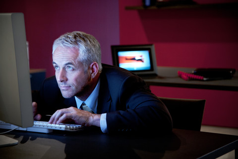 Geschäftsmann sitzt am Schreibtisch und benutzt einen Computer, lizenzfreies Stockfoto