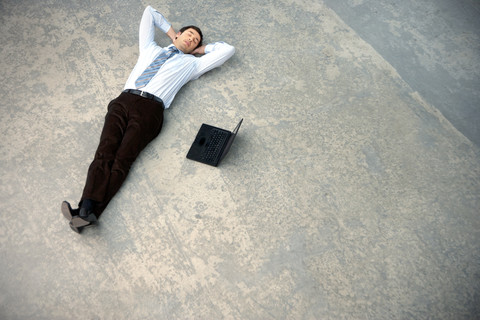 Geschäftsmann auf dem Boden liegend neben einem Laptop, lizenzfreies Stockfoto