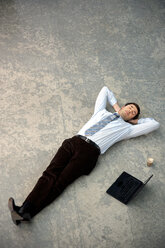 Businessman lying on floor next to laptop - TOYF001243
