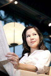 Junge Geschäftsfrau sitzt im Sessel und liest Zeitung - TOYF001256