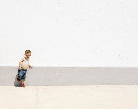 Hemdloser kleiner Junge lehnt an einer Wand, lizenzfreies Stockfoto