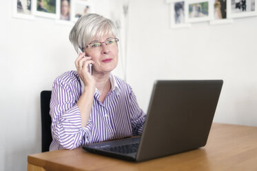 Porträt einer älteren Frau mit Laptop, die mit einem Smartphone telefoniert - FRF000313