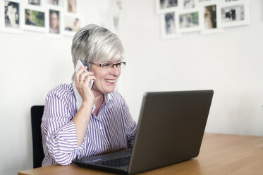 Porträt einer älteren Frau mit Laptop, die mit einem Smartphone telefoniert - FRF000314