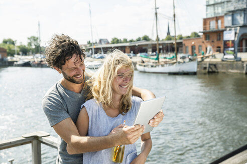 Deutschland, Lübeck, glückliches Paar am Hafen mit digitalem Tablet - FMKF001848