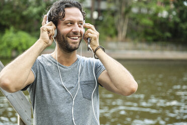 Happy man listening to music at the waterside - FMKF001892