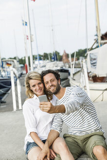 Germany, Luebeck, smiling couple at marina taking a selfie - FMKF001856