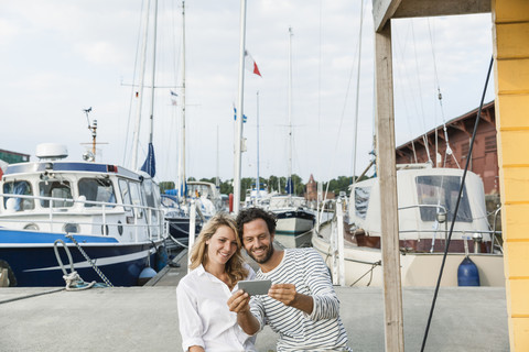 Deutschland, Lübeck, lächelndes Paar am Yachthafen mit Smartphone, lizenzfreies Stockfoto