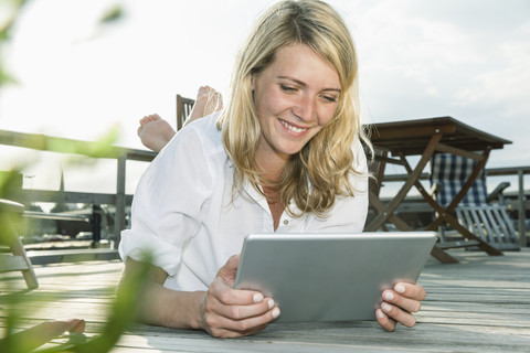 Smiling young woman relaxing on deck using digital tablet stock photo