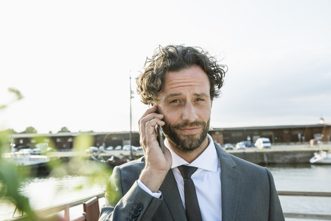 Germany, Luebeck, portrait of businessman at harbor on cell phone stock photo