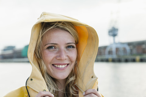 Deutschland, Lübeck, Porträt einer jungen Frau im Regenmantel am Wasser, lizenzfreies Stockfoto