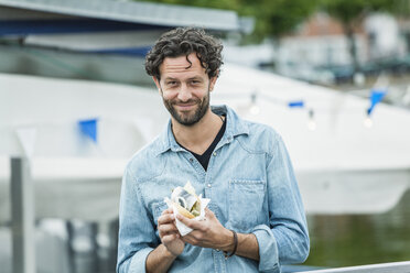 Lächelnder Mann mit einem Fischsandwich in der Hand - FMKF001875