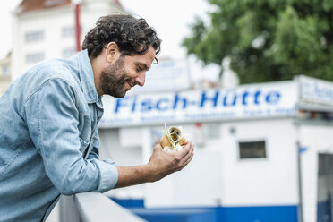 Lächelnder Mann mit einem Fischsandwich in der Hand - FMKF001877