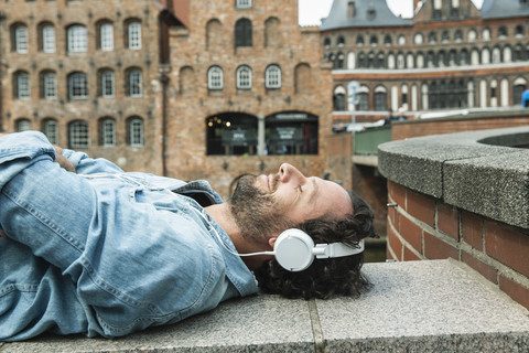 Deutschland, Lübeck, Mann mit Kopfhörern beim Entspannen in der Stadt, lizenzfreies Stockfoto