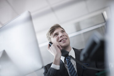 Lächelnder Geschäftsmann, der im Büro telefoniert - ZEF007136