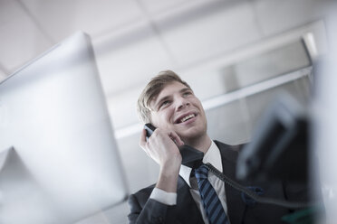 Smiling businessman talking on phone in office - ZEF007136