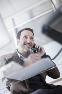 Lächelnder Geschäftsmann, der im Büro telefoniert - ZEF007139