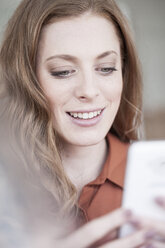 Lächelnde junge Frau schaut auf ihr Handy - ZEF007164