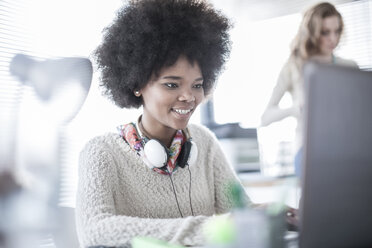 Woman in office working on laptop wearing headphones - ZEF007169