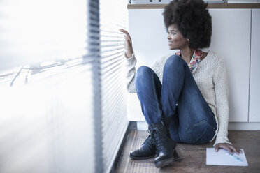 Woman sitting on the floor in office looking out of window - ZEF007173