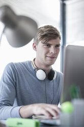 Man at office desk wearing headphones working on laptop - ZEF007175