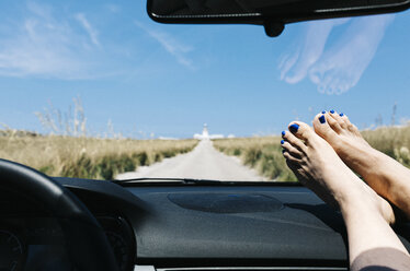 Spanien, Menorca, Füße auf dem Armaturenbrett, Fahren auf leerer Straße im Urlaub mit einem Leuchtturm im Hintergrund - JRFF000004