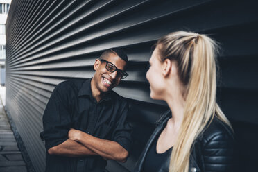 Black dressed young couple standing face to face in front of black facade - CHAF001375