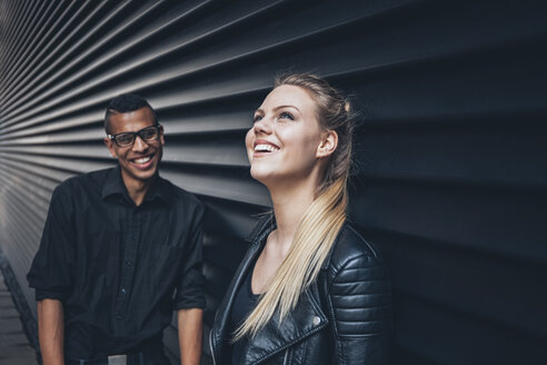 Lachendes junges Paar vor einer schwarzen Fassade - CHAF001377