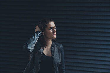 Despaired young woman standing in front of black facade - CHAF001390