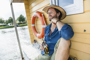 Relaxed man on a house boat with beer bottle - FMKF001939