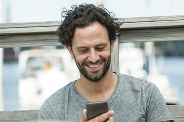 Lächelnder Mann im Freien, der auf sein Handy schaut - FMKF001941