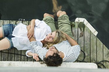 Smiling woman lying on man's lap at the water - FMKF001944