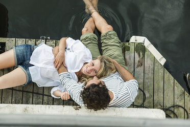 Smiling woman lying on man's lap at the water - FMKF001945