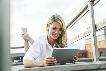 Smiling young woman relaxing on deck using digital tablet - FMKF001948