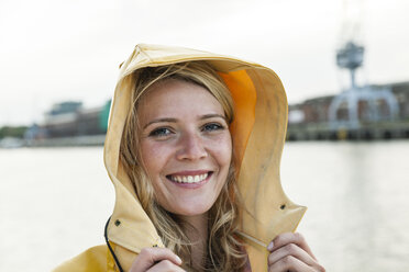 Portrait of young woman wearing rain coat at the waterside - FMKF001954