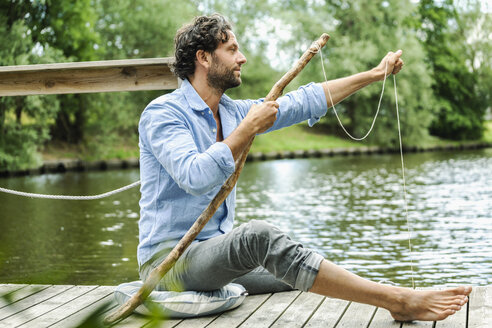 Mann sitzend auf Plattform am Wasser mit selbstgebauter Angelrute - FMKF001962